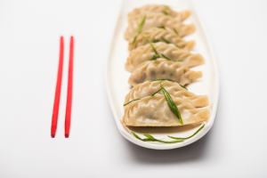 dumplings on a long white plate with red chopsticks laying to the side