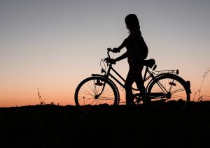 a girls silhouette with her bike at sunset