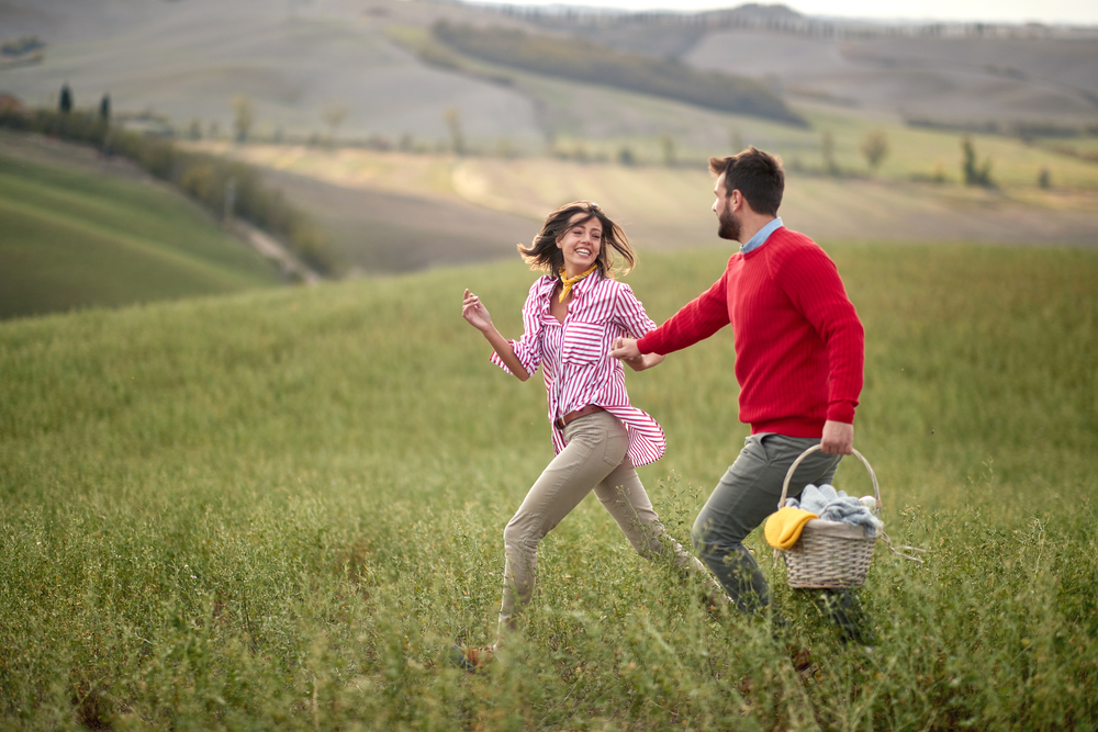 2 people walking across a grassy field with a picnic basket