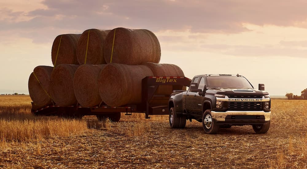A black 2021 Chevy Silverado 3500 HD is shown from the front at an angle while towing bales of hay.