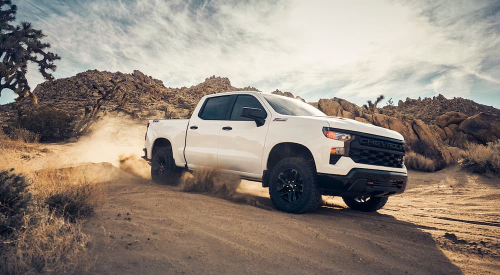 A white 2024 Chevy Silverado 1500 Custom is driving on a desert trail.