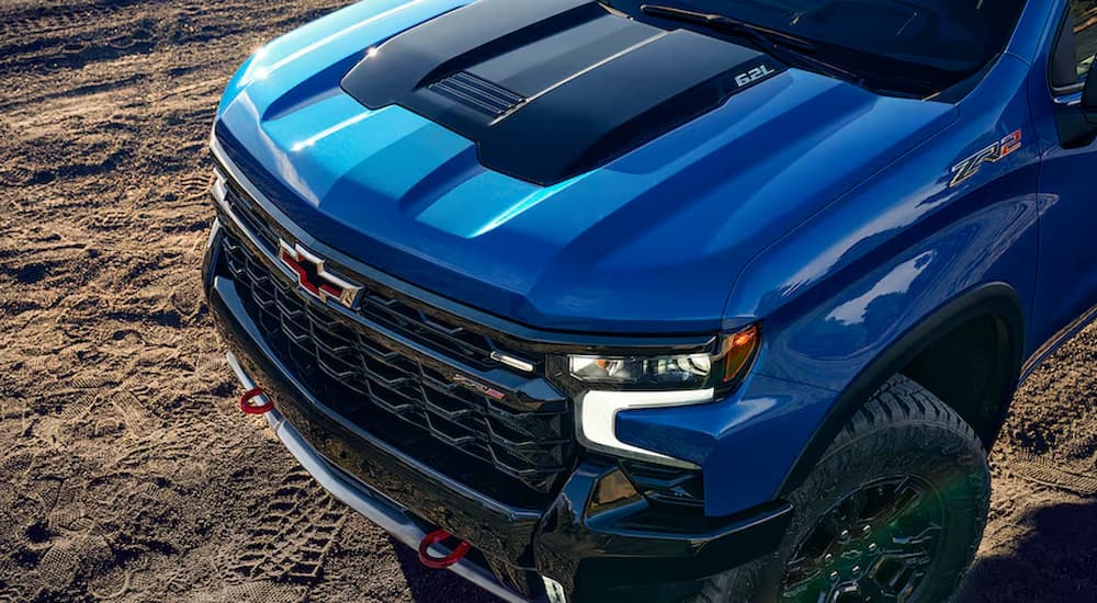 A close up of the hood of a blue 2024 Chevy Silverado 1500 ZR2 parked on dirt.