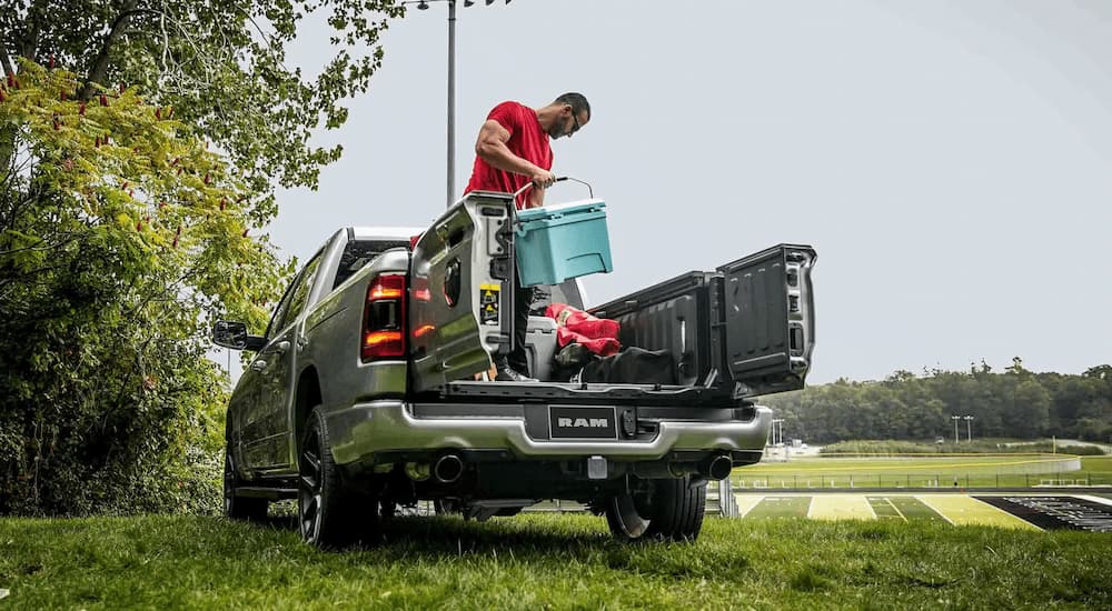 A man is standing in the bed of a silver 2024 Ram 1500.