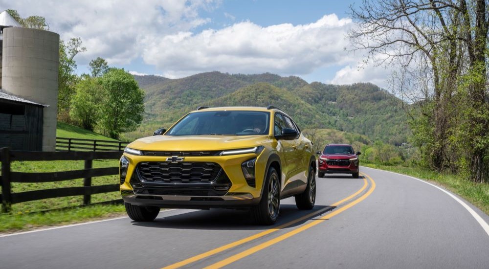 A yellow 2024 Chevy Trax ACTIV driving by a fence followed by a red 2024 Chevy Trax RS.
