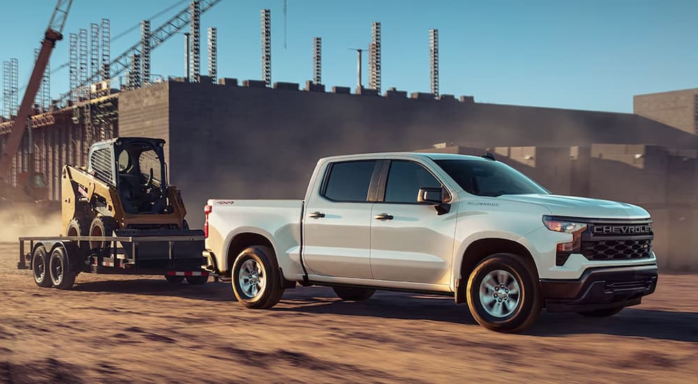 A white 2025 Chevy Silverado 1500 WT towing heavy machinery at a construction site.