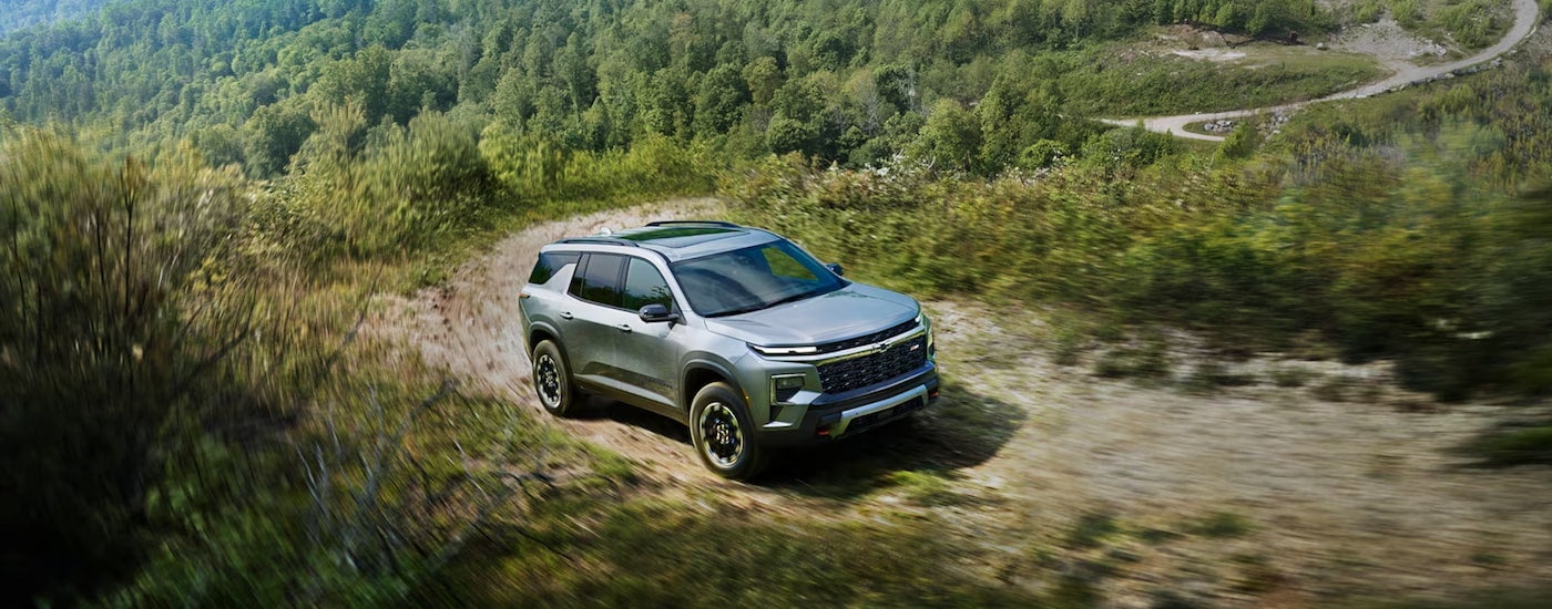 A silver 2024 Chevy Traverse Z71 driving up a mountain on a dirt trail.